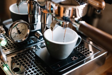 Siebträger-Kaffeemaschine befühlt Tasse mit frisch gebrühten Kaffee.
